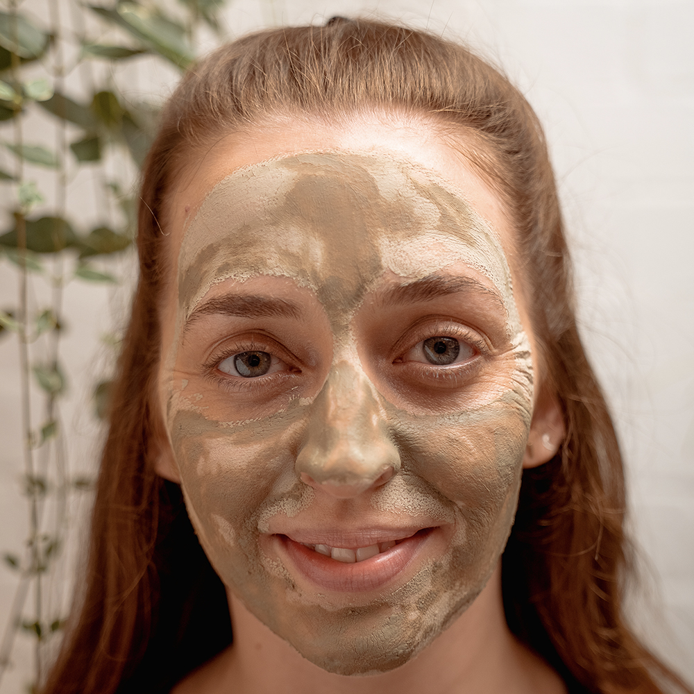 Person with clay face mask smiling.