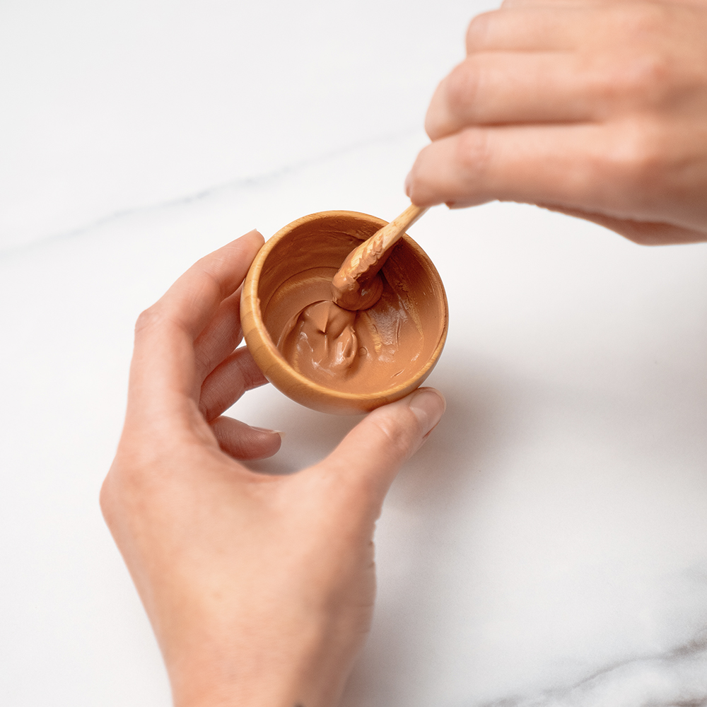 Hands mixing clay in small bowl.
