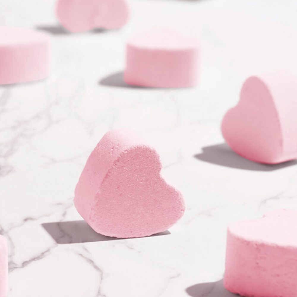 Pink heart-shaped bath bombs on marble surface.
