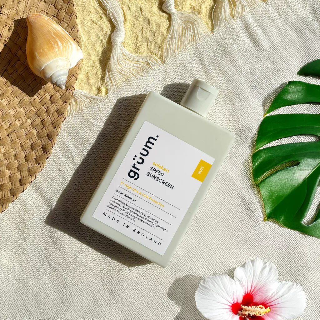 Sunscreen bottle on sand with shell and leaf.