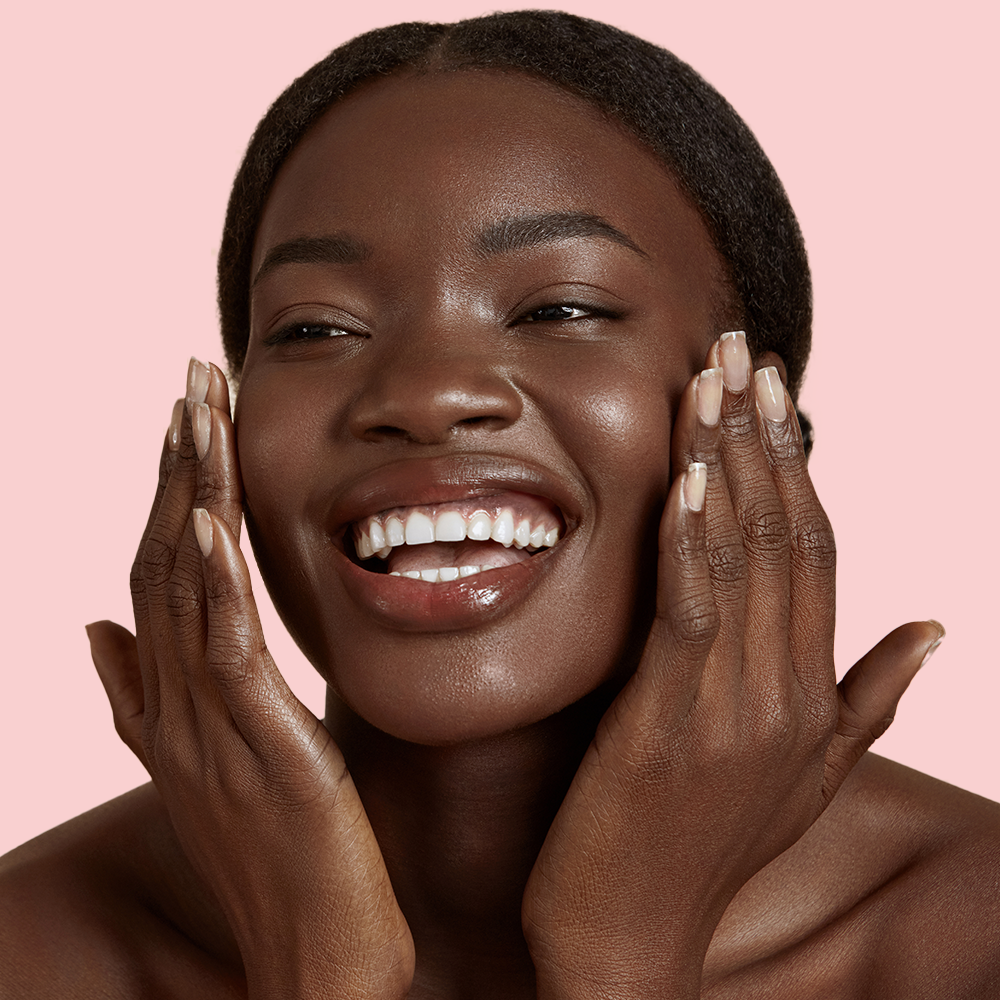 Smiling person touching face against pink background.