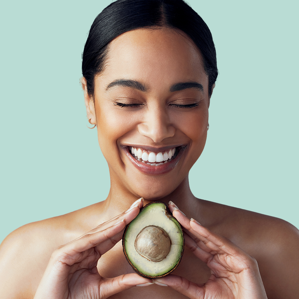 Smiling person holding half an avocado