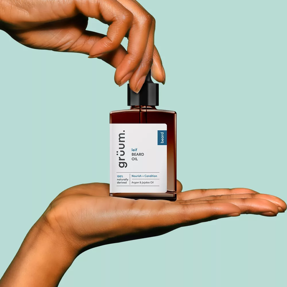 Hands holding a beard oil bottle.